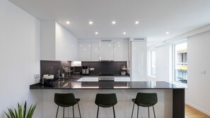 A modern kitchen with white cabinets, a black countertop, and three green bar stools. - Morro Premium Apartment w/ Free Parking (Vila Nova de Gaia)