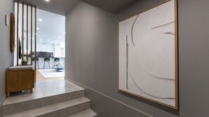 A modern interior with a staircase leading to a dining area, a minimalist artwork on the wall, and a wooden cabinet with a plant. - Morro Premium Apartment w/ Free Parking (Vila Nova de Gaia)