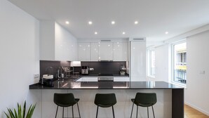 A modern kitchen with white cabinets, a black countertop, and three green bar stools. - Morro Premium Apartment w/ Free Parking (Vila Nova de Gaia)