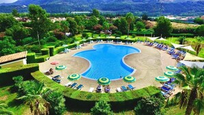 Una gran piscina circular rodeada de sillas de descanso y sombrillas, con un jardín ajardinado y colinas en la distancia.