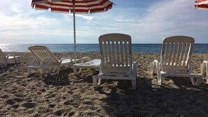 Une plage avec des chaises longues blanches et un parasol à rayures rouges et blanches.