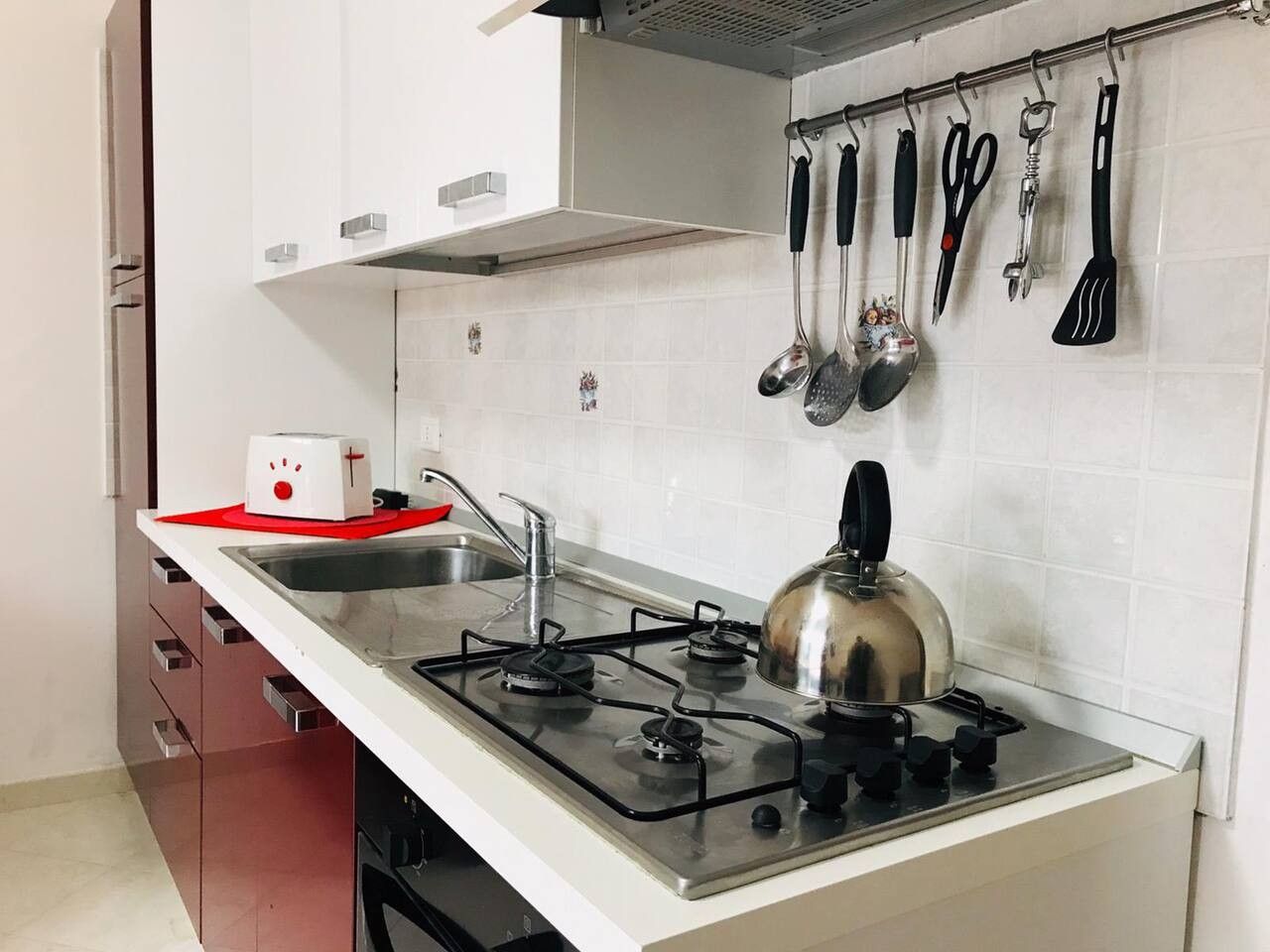 Une cuisine équipée d’une cuisinière à gaz, d’une bouilloire et de divers ustensiles de cuisine accrochés au mur.