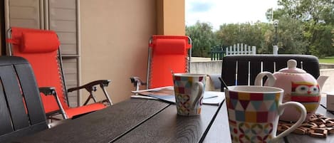 A table with two chairs, a teapot, and two mugs.