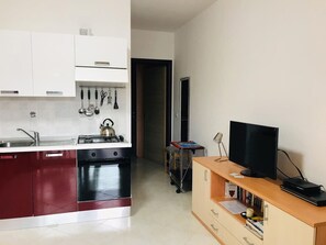 Una cocina moderna con estufa, horno y pileta. Hay un televisor sobre un mueble de madera y un carrito con objetos.