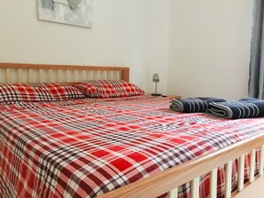 Una cama con colcha a cuadros, una lámpara de noche y toallas enrolladas al lado.