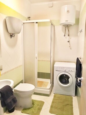 Un baño pequeño con inodoro, cabina de ducha, lavadora y secador de manos.