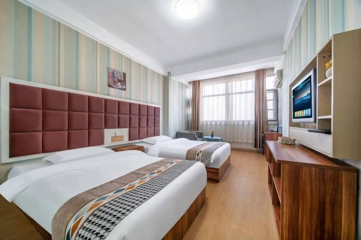 A hotel room with two beds, a TV, a desk, and a window with curtains.
