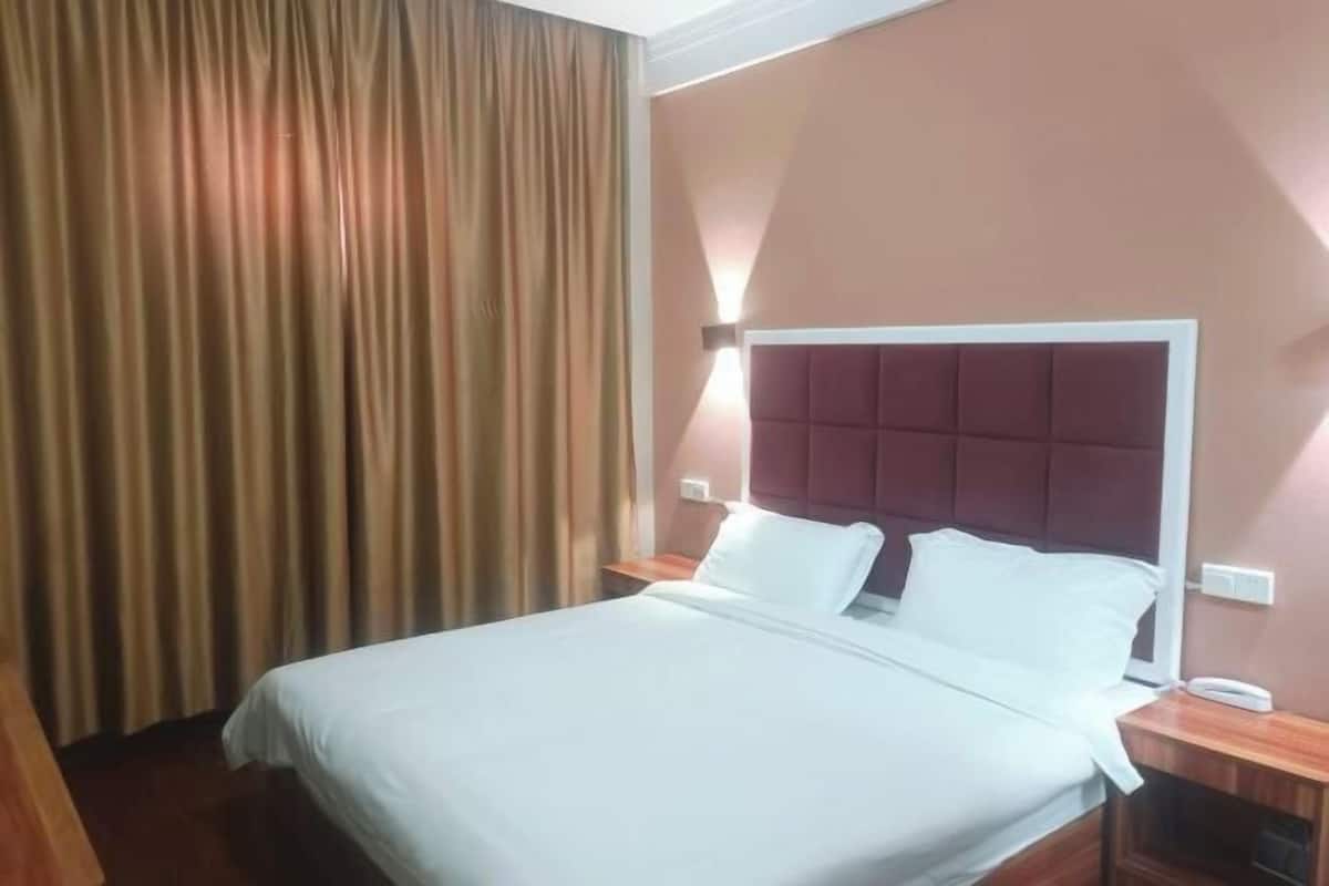 A hotel room with a bed, curtains, a wall-mounted light, and a bedside table.