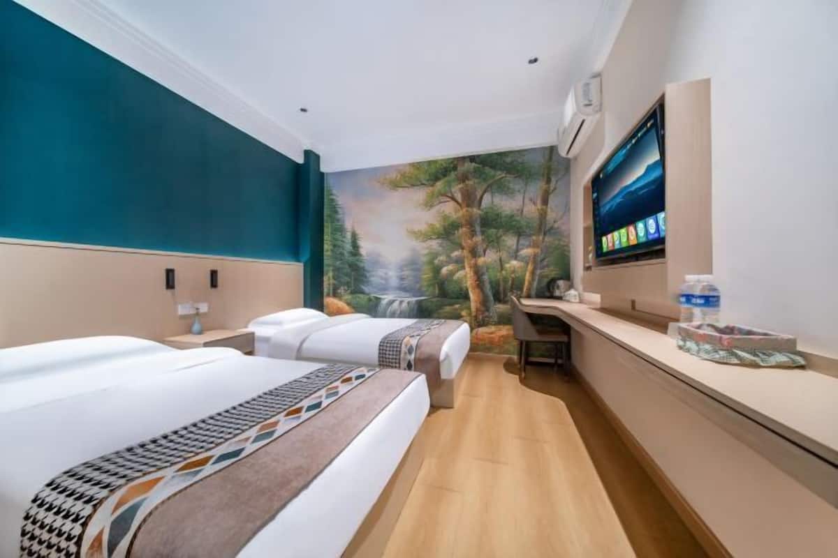 A hotel room with two beds, a desk, a TV, and a mural of a forest scene.