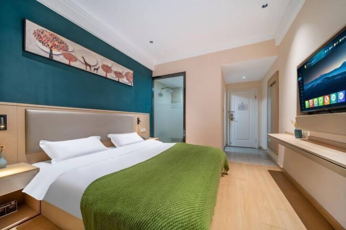 A modern hotel room with a large bed, a flat-screen TV, and a painting on the wall.
