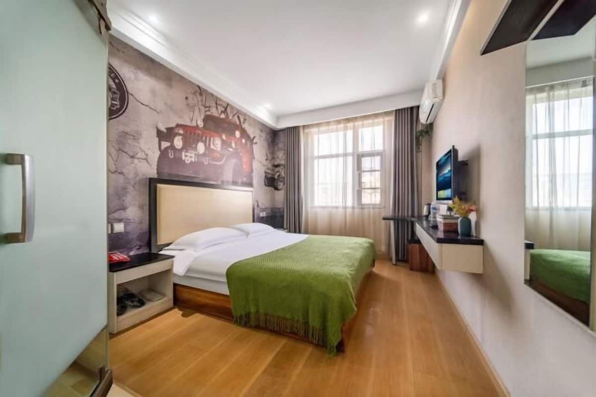 A hotel room with a bed, a desk, a TV, and a mural on the wall.