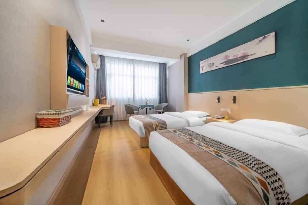 A hotel room with two beds, a desk, a chair, a TV, and a painting on the wall.