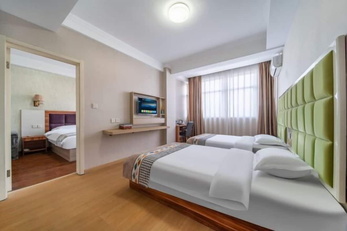A hotel room with two beds, a television, a desk, and a window with curtains.