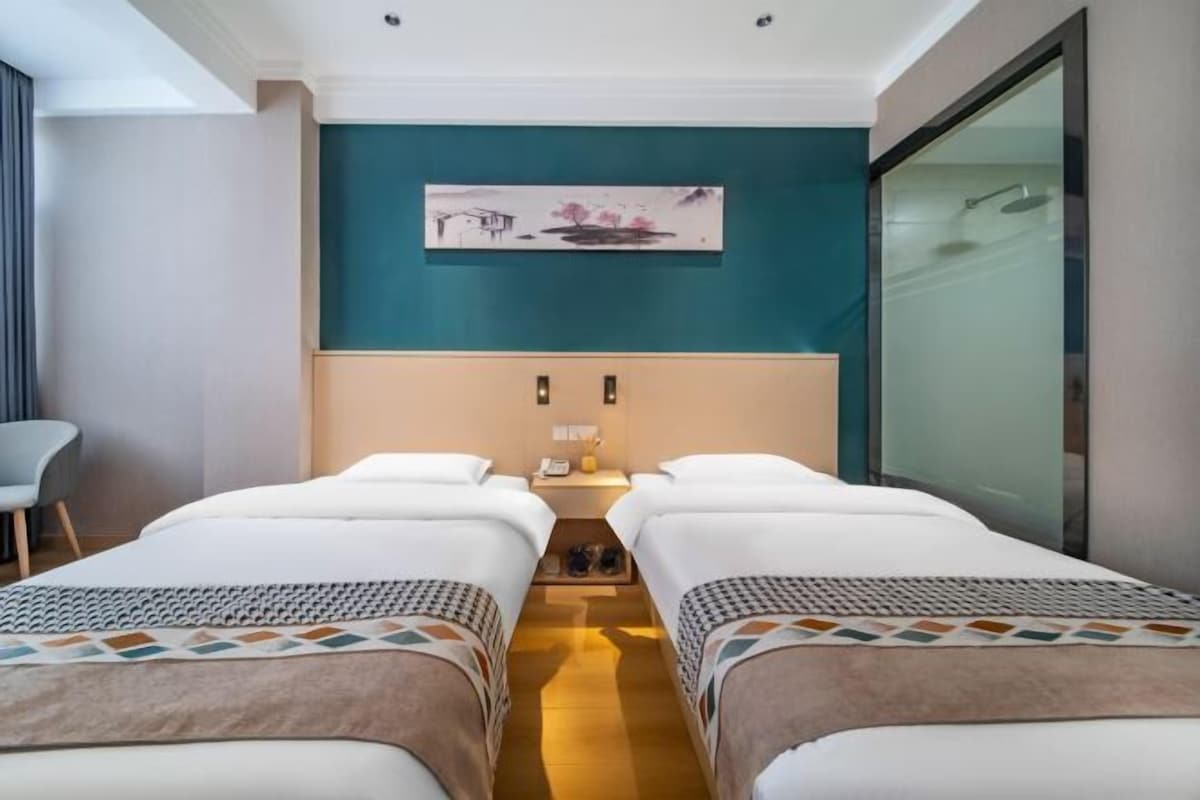 Une chambre d’hôtel avec deux lits, un bureau, une chaise et un tableau au mur.