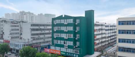 Un edificio de varios pisos con fachada verde, rodeado de otros edificios y árboles.
