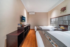 Une chambre d’hôtel avec un plancher en bois, un bureau doté d’un téléviseur à écran plat, un lit recouvert d’une couvre-lit à motifs et une tête de lit au design texturé.