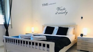 A bedroom with a white bed, black and white pillows, a nightstand with a lamp, and a wall with motivational quotes. - Pizzo Beach Club 57F Two Bedroom (PIZZO)