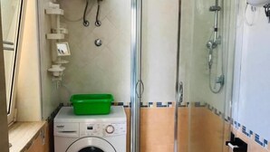 Een praktische badkamer met een wasmachine, een douchecabine van glas en een toilet.