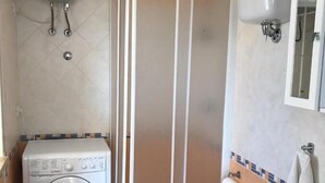 Een kleine badkamer met een wasmachine, toilet en douchecabine.
