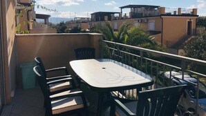 Een balkon met een tafel en stoelen, met uitzicht op een woongebied met gebouwen en een heldere lucht.