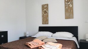 Een netjes opgemaakt bed met een bruine deken met patroon en twee kussens, een nachtkastje met een lamp, en een kunstwerk boven het bed.