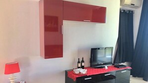Una habitación con televisor sobre un mueble negro, una lámpara roja y una cortina roja.