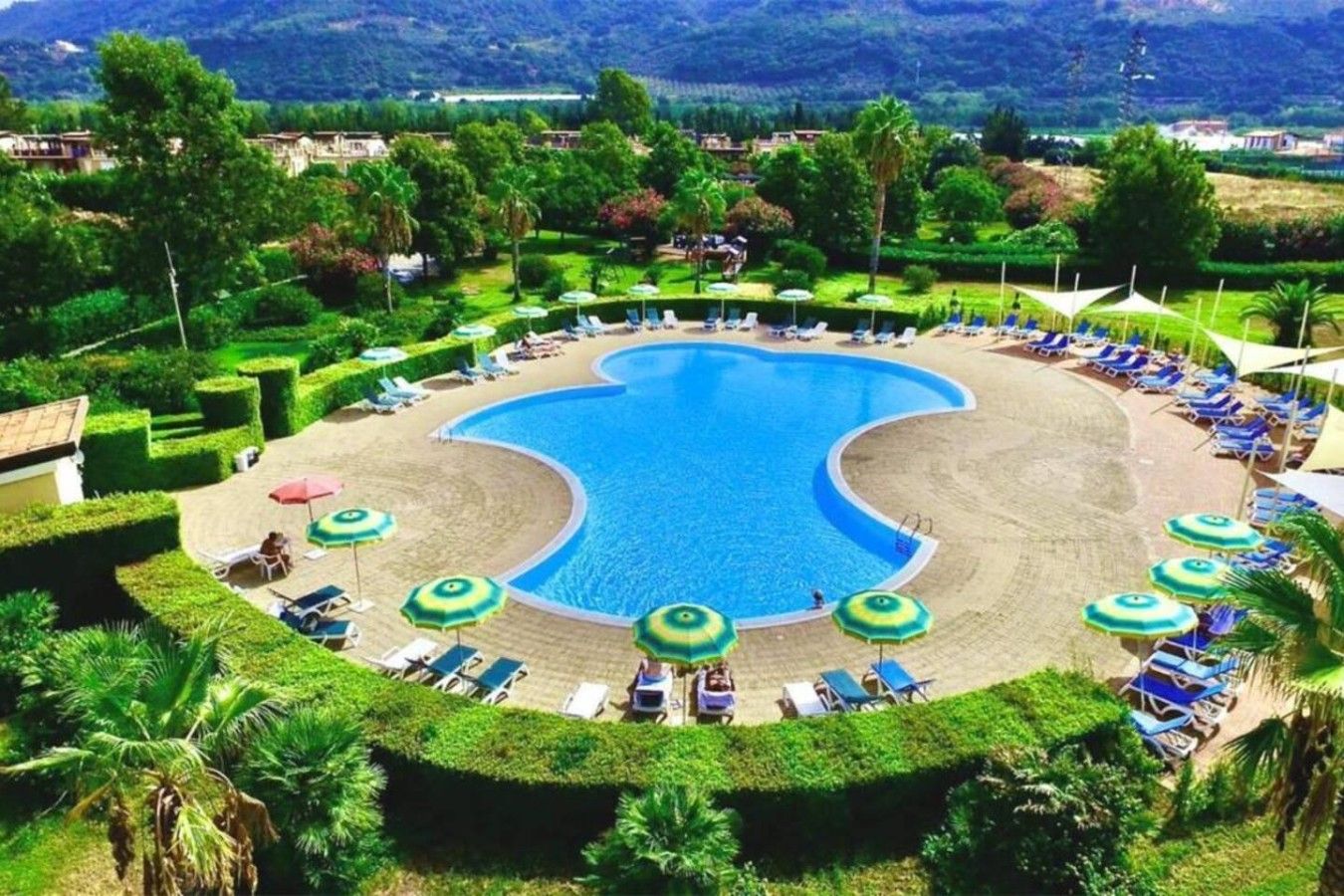 Ein Resort mit einem großen zentralen Schwimmbecken, Liegestühlen und Palmen.