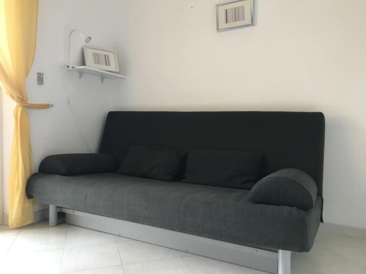 En grå soffa med en vit botten, en gul gardin och en inramad tavla på väggen.