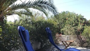 Twee blauwe fauteuils met witte kussens, een klein houten tafeltje met een lamp, en een palmboom op de achtergrond.