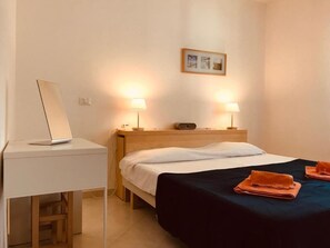 Habitación de hotel con cama, lámparas de noche, un escritorio con una computadora portátil y una toalla doblada sobre la cama.