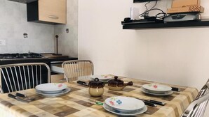 Una mesa de comedor dispuesta con platos, tazones y teteras, rodeada de sillas.