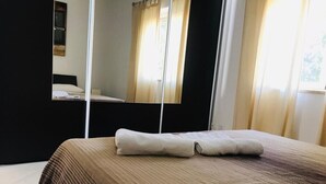Una cama bien hecha con una colcha marrón y beige a rayas, una toalla blanca y un espejo que refleja una ventana con cortinas.