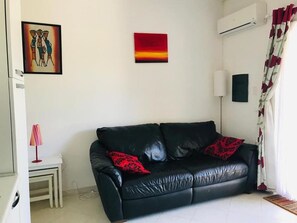 A living room with a black leather sofa, a small side table with a lamp, and artwork on the walls. - Pizzo Beach Club One Bedroom 67 (PIZZO)