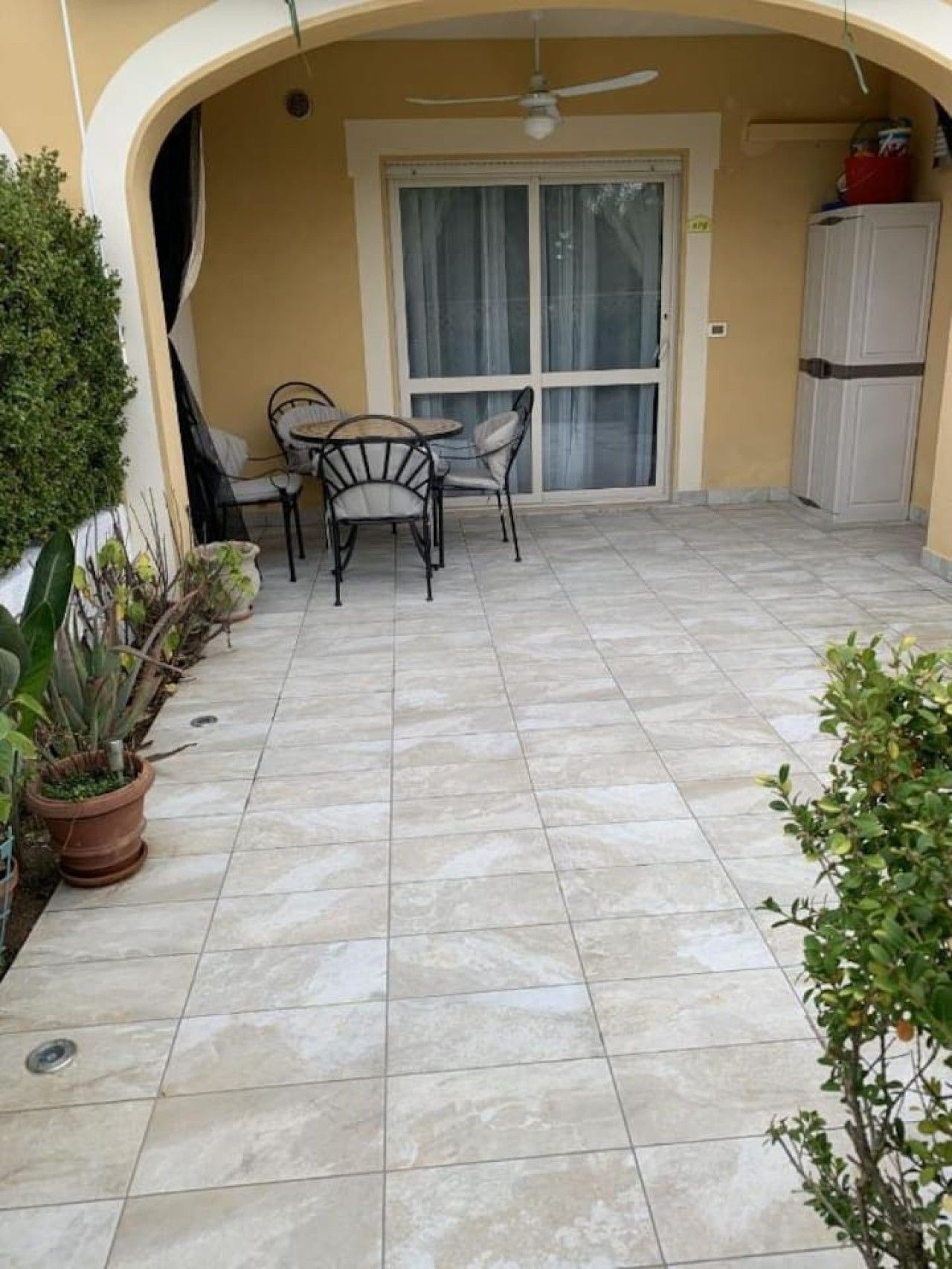 Un espace patio aménagé avec une table et des chaises, un ventilateur de plafond et une porte-fenêtre coulissante.