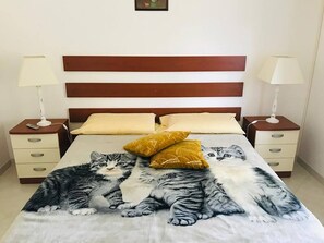A bed with a cat-themed bedspread, two bedside tables with lamps, and a headboard. - Pizzo Beach Club One Bedroom 67 (PIZZO)