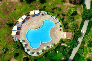An aerial view of a resort with a central swimming pool surrounded by sun loungers and umbrellas, a small building, and a well-maintained lawn. - Pizzo Beach Club One Bedroom 67 (PIZZO)