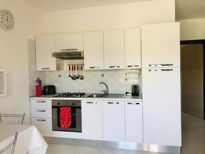 A modern kitchen with white cabinets, stainless steel appliances, and a red polka-dotted oven mitt. - Pizzo Beach Club One Bedroom 67 (PIZZO)
