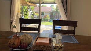Zona pranzo con due sedie di legno, un tavolo con un centrotavola a forma di zucca, un portatessuti e vista su un giardino attraverso una porta in vetro.