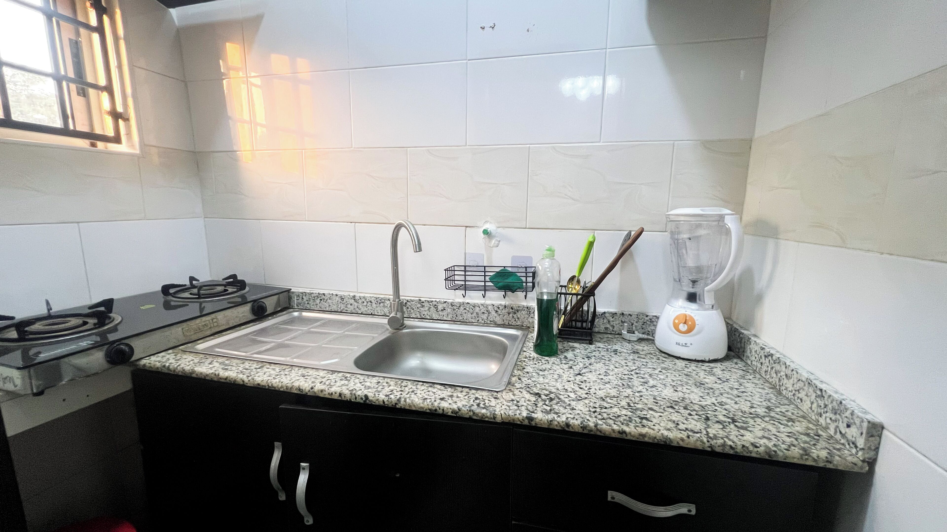 A kitchen with a gas stove, a sink, a blender, and a window.