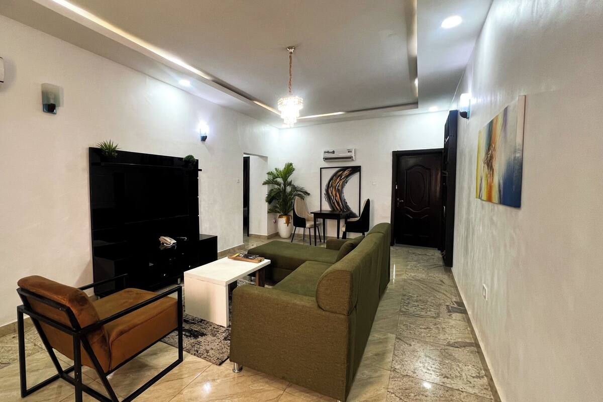 A living room with a sofa, a chair, a TV, a table, and a plant.