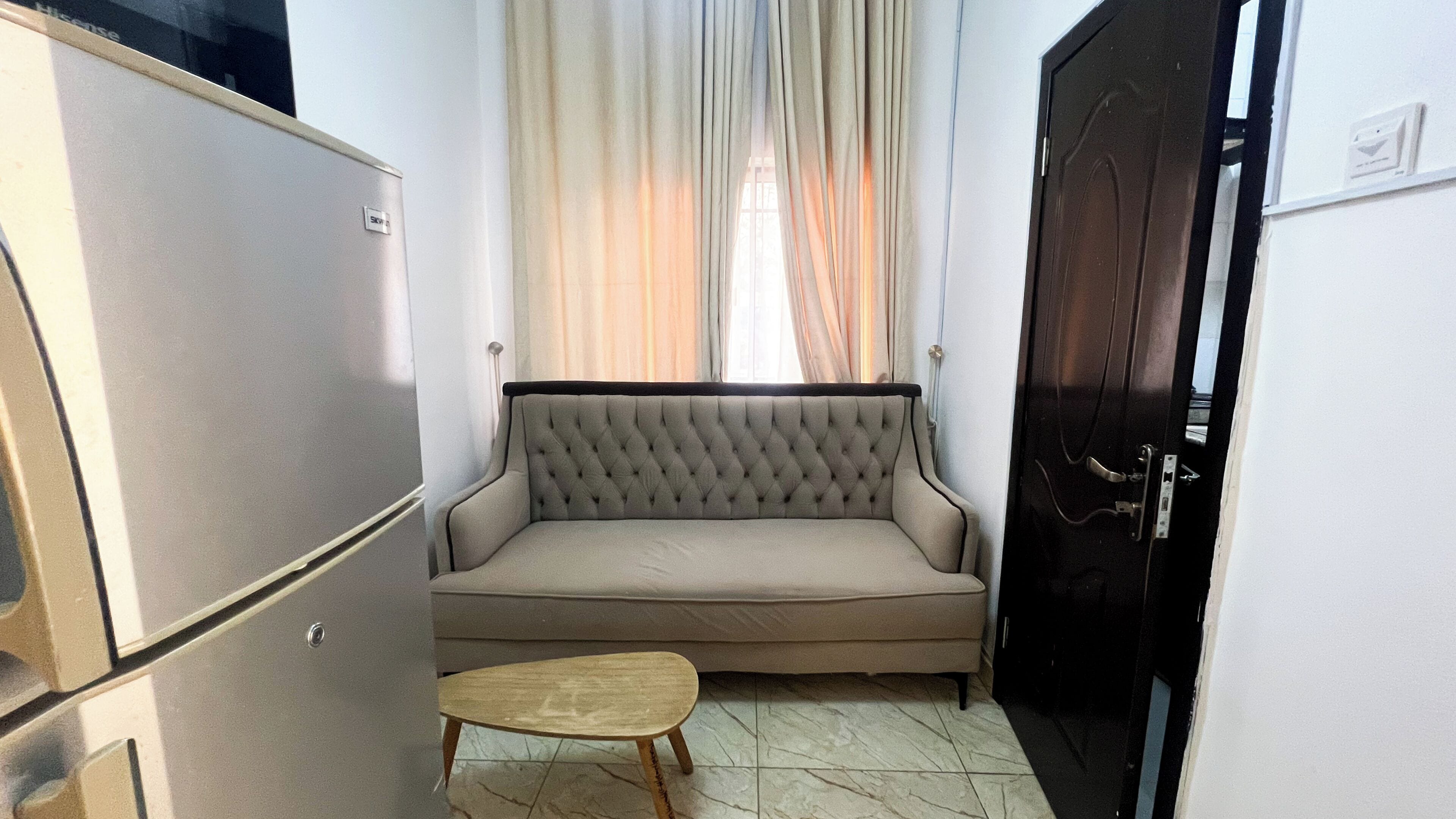 A compact living space with a sofa, a small wooden stool, and a closed door.