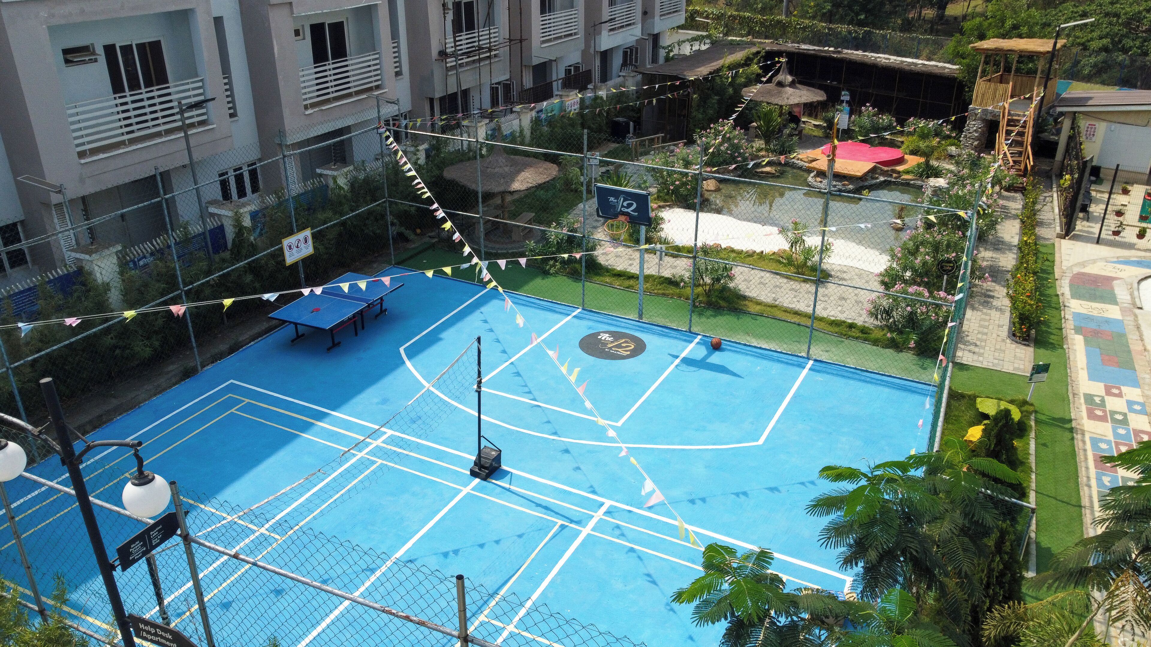 Ein blauer Tennisplatz, umgeben von einem Maschendrahtzaun, mit einem Basketballkorb und einem Tennisnetz.