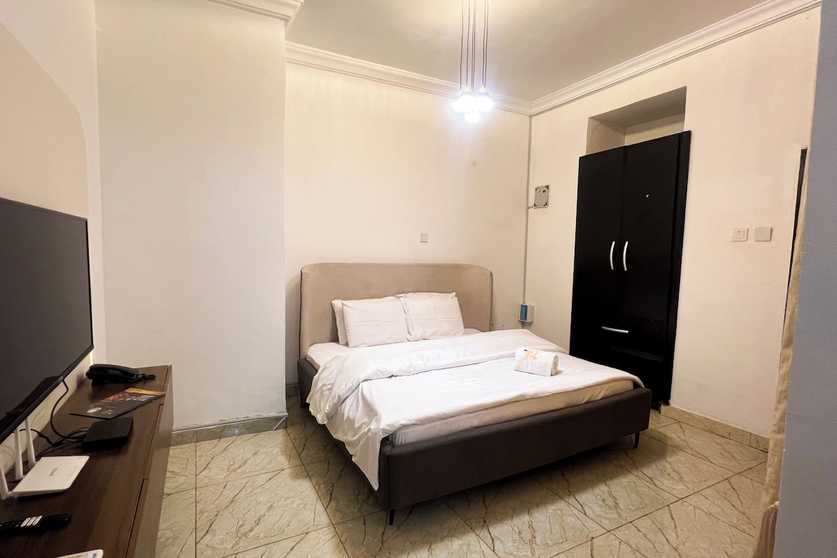 A bedroom with a bed, a TV, a desk, and a wardrobe.