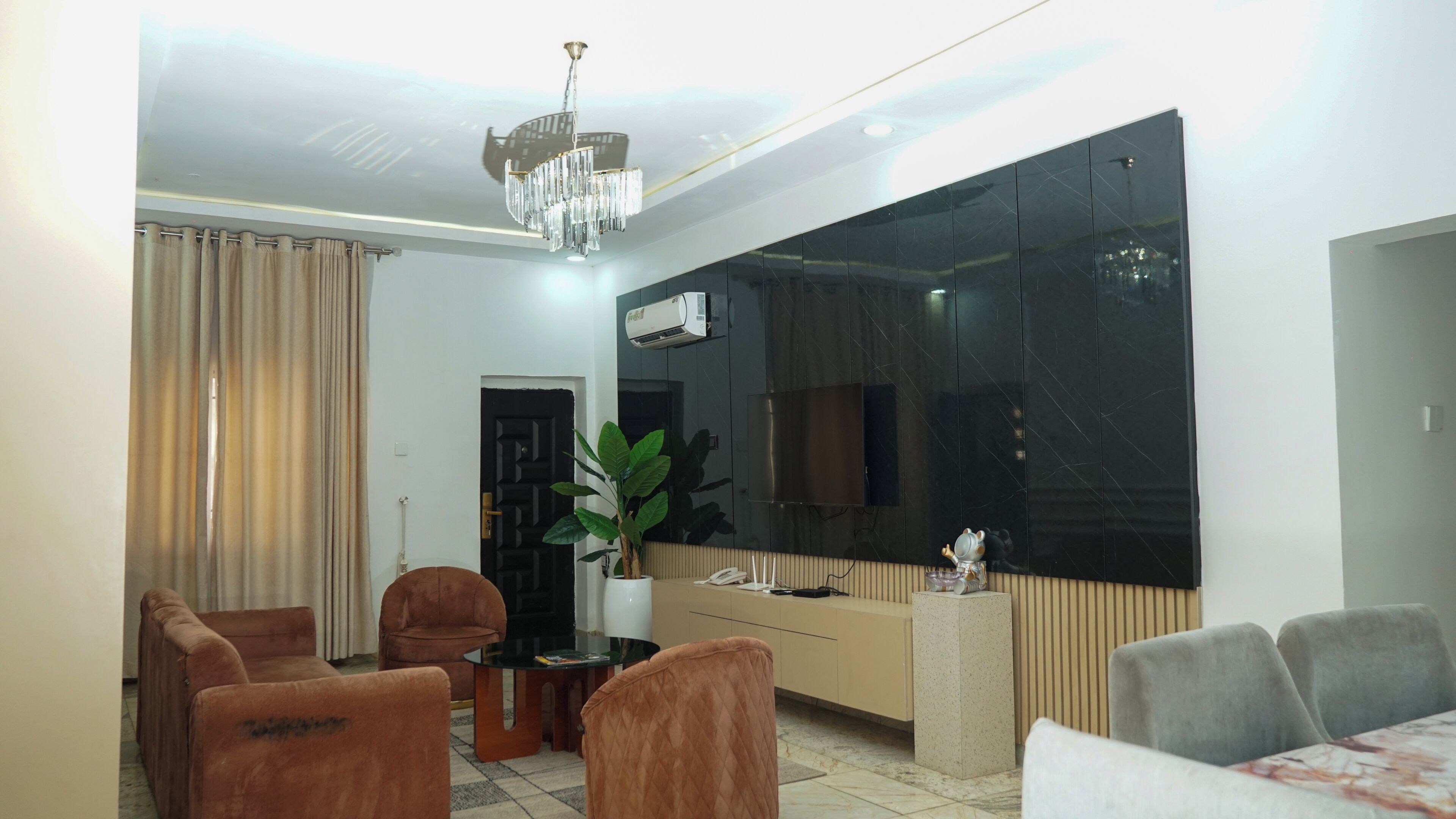 A living room with a large flat-screen TV, a chandelier, a potted plant, and a sofa.