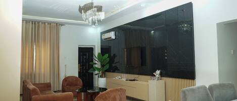 A living room with a large flat-screen TV, a chandelier, a potted plant, and a sofa.