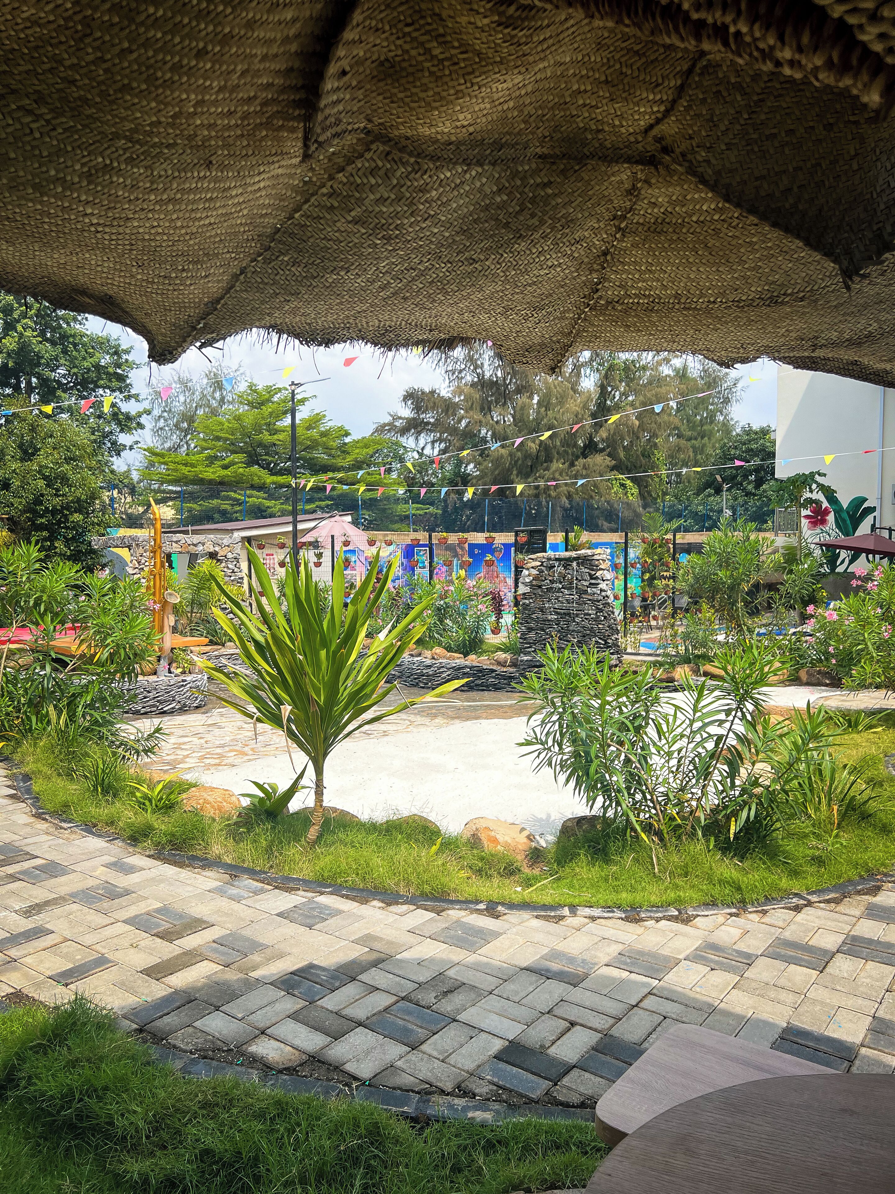 A garden area with a thatched roof structure, paved walkway, and various plants.