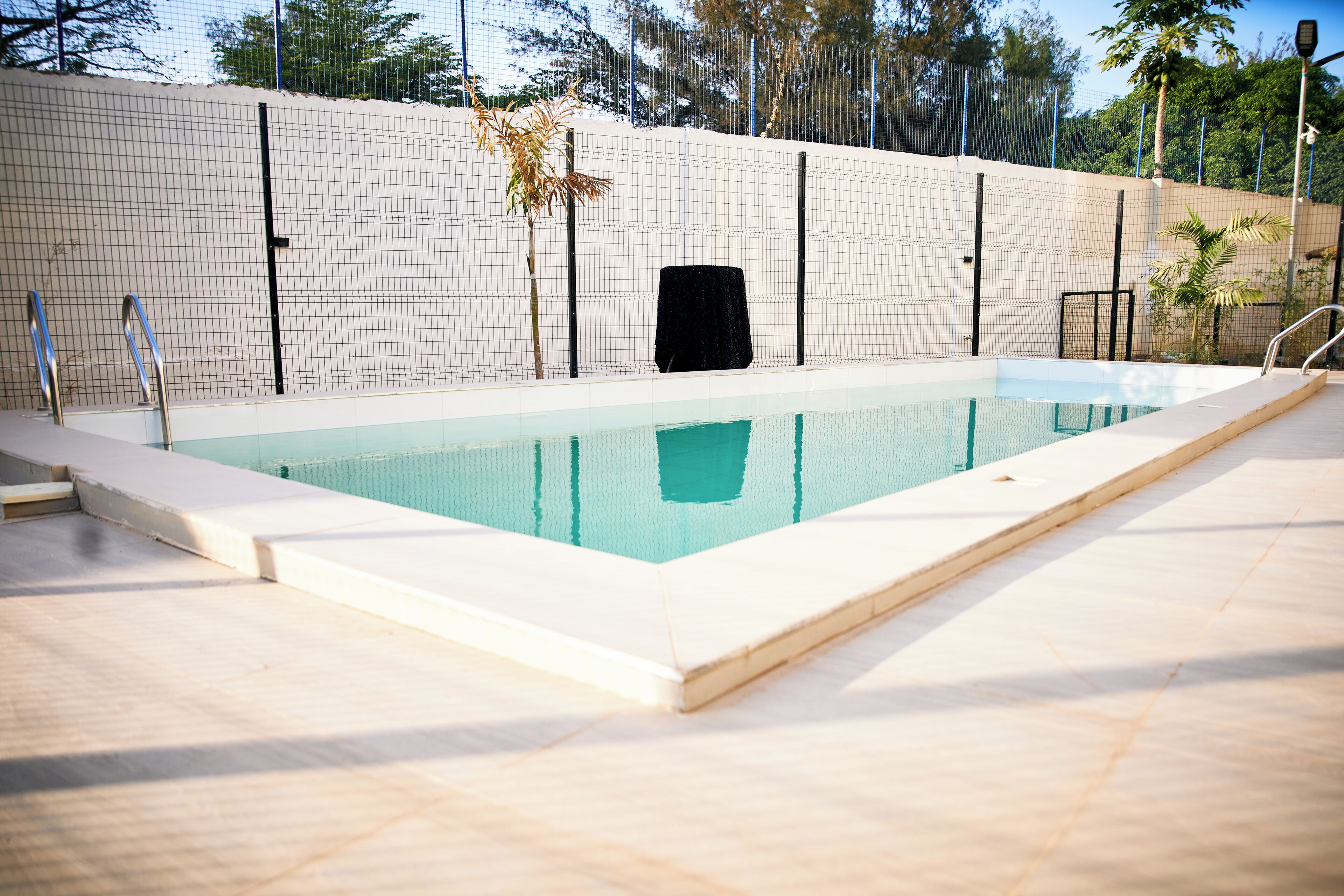 Una piscina rectangular con borde de azulejos, rodeada por una valla y un muro de cerámica.