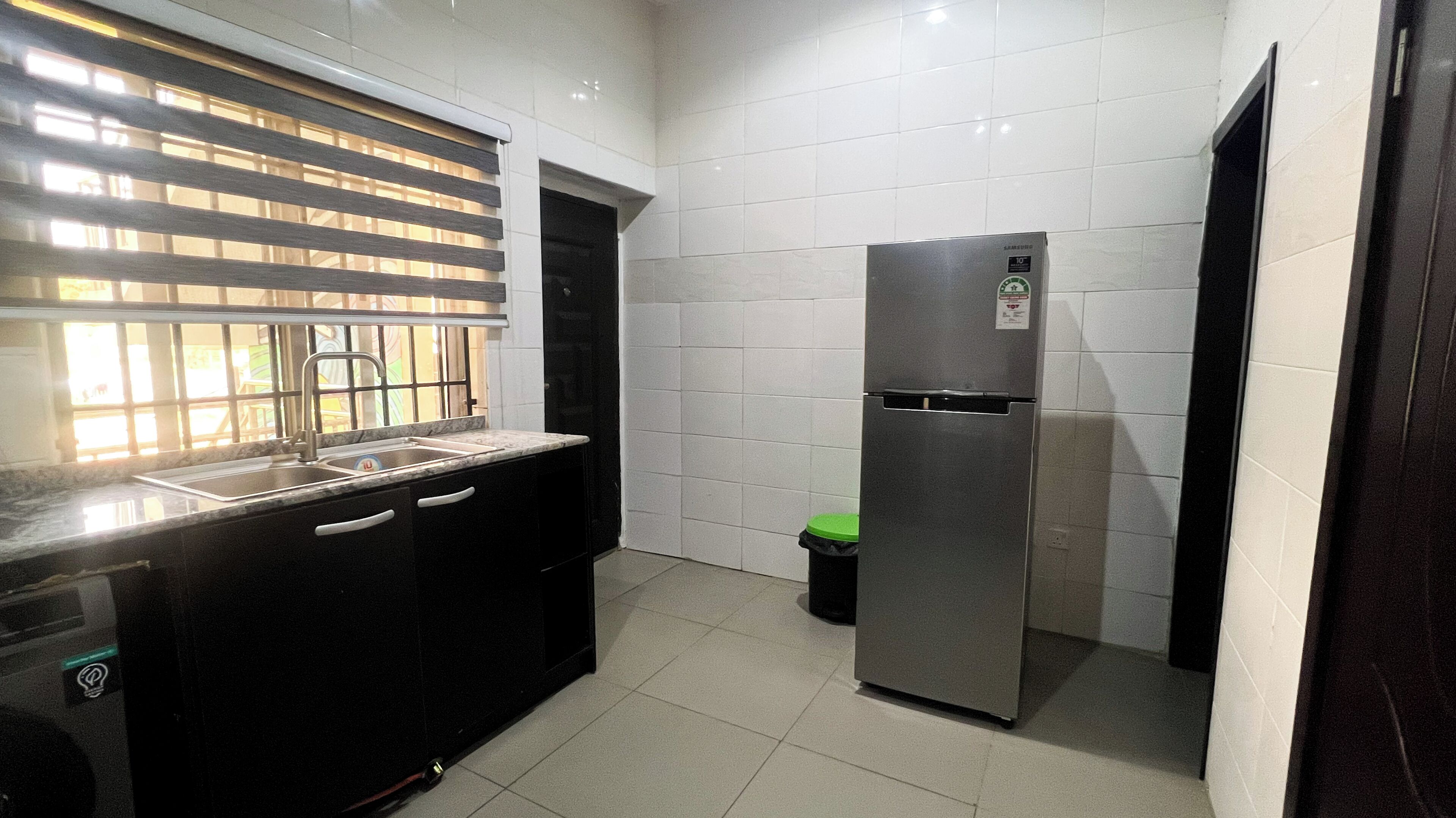 Una cocina compacta con un refrigerador de acero inoxidable, un lavamanos con grifo y una ventana con persianas.