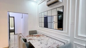 Een eetgedeelte met een marmeren tafel, grijs gestoffeerde stoelen en een airconditioner aan de muur.