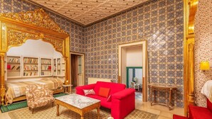 A room with a red sofa, a wooden coffee table, a wicker chair, and a bookshelf. - La Demeure Médina (Tunis)
